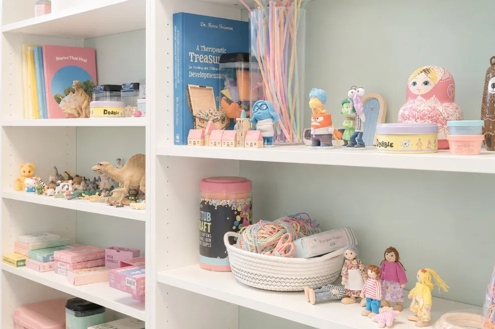 Open shelves holding books, creative materials and therapeutic resources